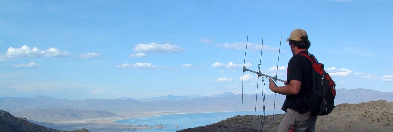 man tracking wildlife with radio telemetry equipment, holding a Yagi antenna atop a mountain.